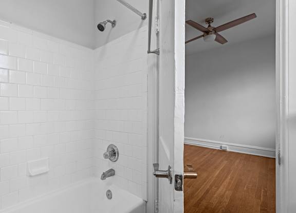 A white tiled bathroom with a wooden floor and a ceiling fan.