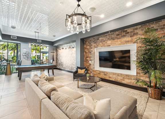 A living room with a large couch and a flat screen TV mounted on a brick wall.