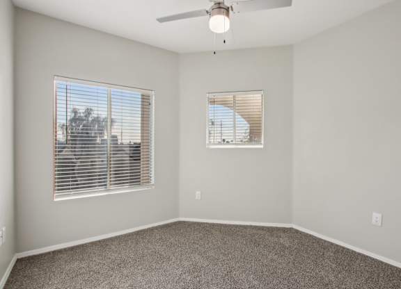 A room with a ceiling fan and two windows at Sweetwater At Metro North Apartments, Phoenix