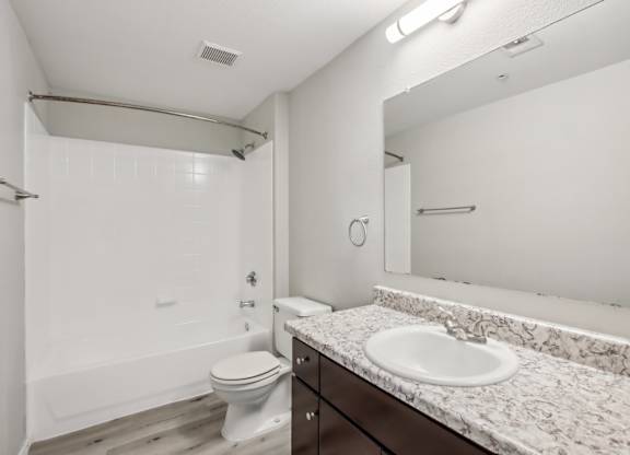 A white bathroom with a toilet, sink, and mirror at Sweetwater At Metro North Apartments, Phoenix, Arizona