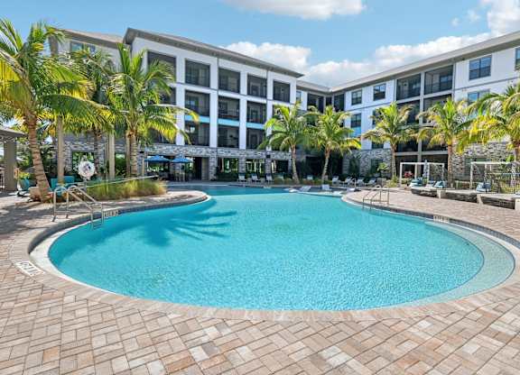 A large swimming pool surrounded by palm trees and a building in the background.