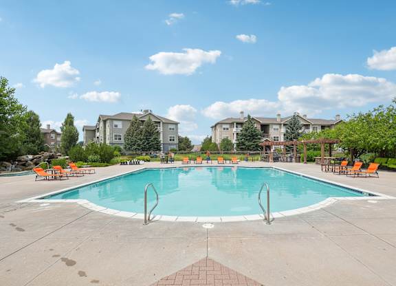 A swimming pool surrounded by orange chairs and trees.