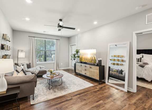 A well-lit, modern living room with a grey couch, a coffee table, and a large mirror.