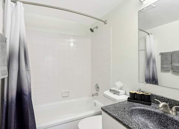 A bathroom with a white tub, sink, and grey tiles. at Millennium at Creve Coeur, Creve Coeur, 63141