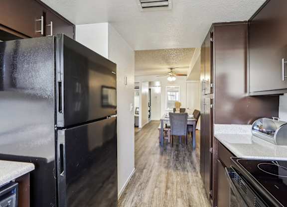 A kitchen with a black refrigerator and brown cabinets.