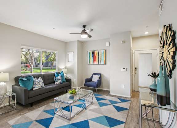 A living room with a grey couch, a blue chair, and a glass coffee table at Sweetwater At Metro North Apartments, Phoenix, AZ
