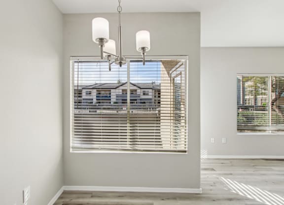 A room with a large window covered by white blinds and a chandelier hanging from the ceiling at Sweetwater At Metro North Apartments, Phoenix