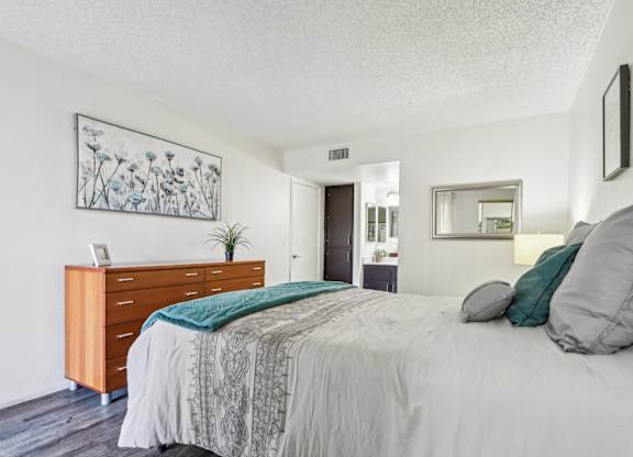 A bedroom with a bed, nightstand, and a plant.