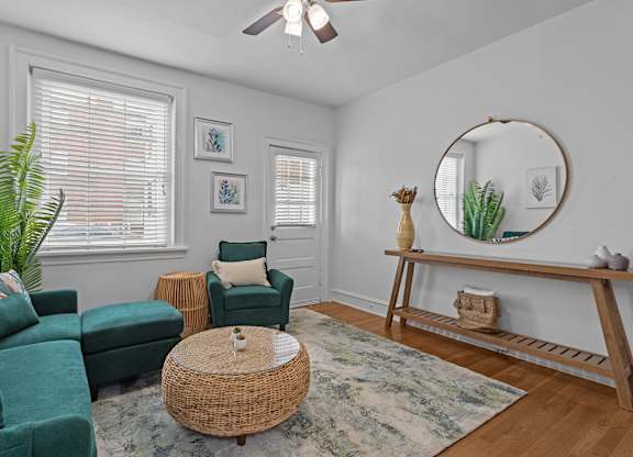 A living room with a green couch, a wicker table, and a mirror on the wall.