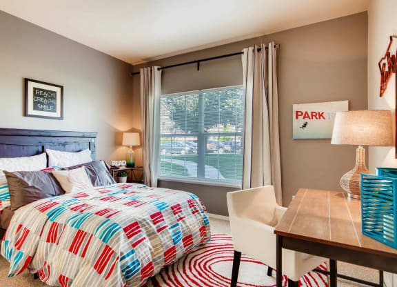 a bedroom with a bed and a desk with a window at Heritage at Stone Mountain, Northglenn, CO, 80233