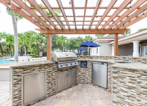an outdoor kitchen with a pergola and a pool in the background at Heritage Bay, Florida, 34957