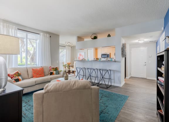 a living room with a kitchen in the background and a couch and chair in the foreground at Heritage Bay, Jensen Beach, FL 34957