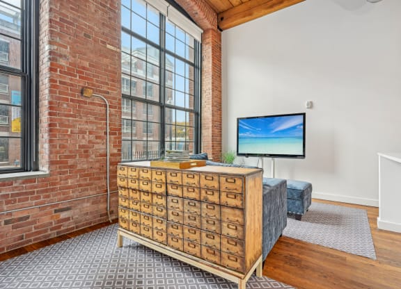 a living room with a large window and a dresser with a tv on it at Riverwalk Apartments, Lawrence, MA