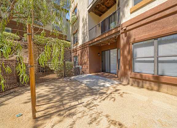 A sandy courtyard with a building and a tree in the background.