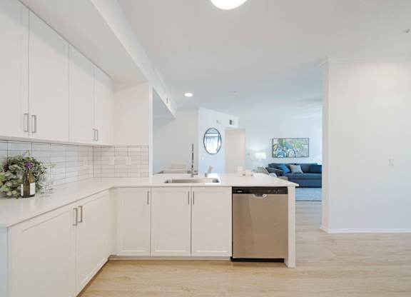 A kitchen with white cabinets and a trash can.