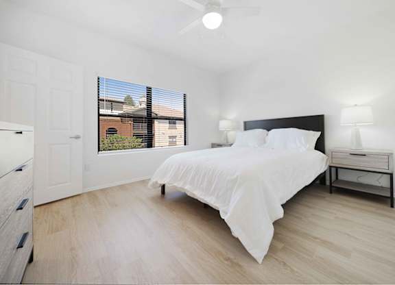 A bedroom with a bed, nightstand, and window with blinds.