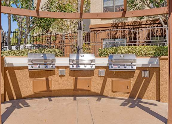 Three barbecue grills are lined up on a patio.