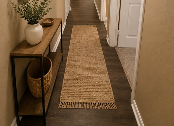 A hallway with a rug on the floor and a plant on a shelf.