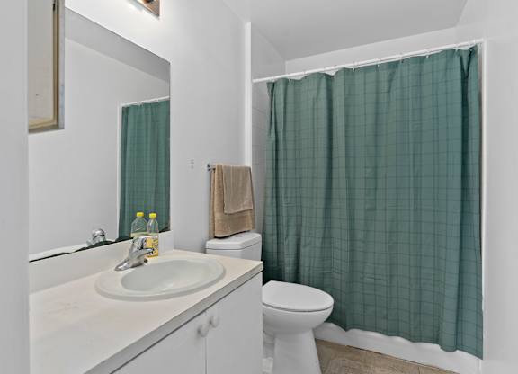 a bathroom with a green shower curtain and a toilet and sink at The Groves at Wimauma Apartments , Florida