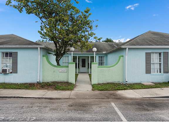 a white and green house with a tree in front of it at The Groves at Wimauma Apartments , Wimauma, FL, 33598