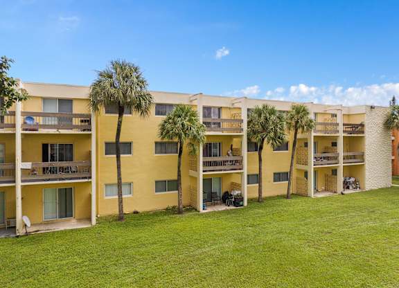 a large yellow apartment building with palm trees in front of it at Cypress Grove, Lauderhill, 33313