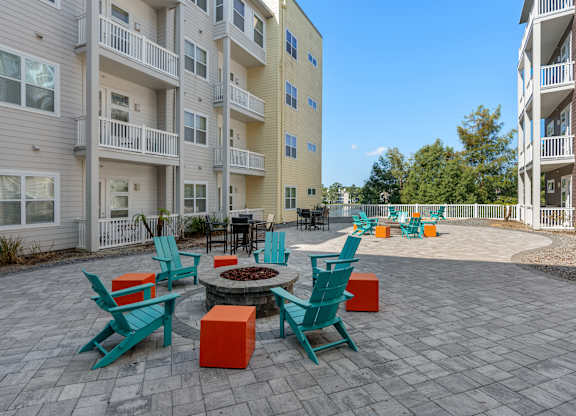 an outdoor patio with chairs and a fire pit in front of an apartment building at Lake Lofts at Deerwood, Jacksonville