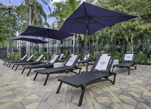 a row of lounge chairs with umbrellas in front of a fence  at Club at Emerald Waters, Hollywood