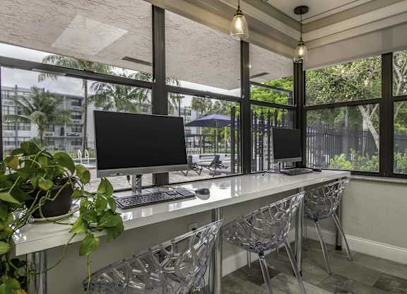 two computer monitors on a long desk in front of a window  at Club at Emerald Waters, Florida