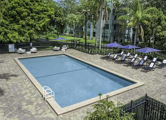 a swimming pool with lounge chairs and umbrellas in front of an apartment building  at Club at Emerald Waters, Hollywood, FL