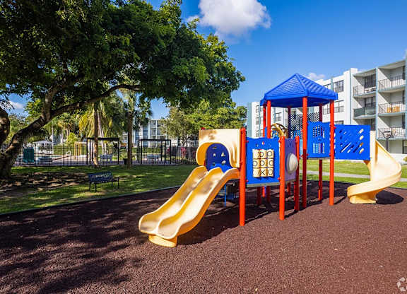 a playground with a slide and monkey bars in front of an apartment building  at Club at Emerald Waters, Hollywood, FL