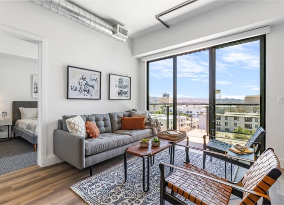 Cozy living room decorated with a gray couch, brown leather table and chairs by a beautiful outdoor balcony.