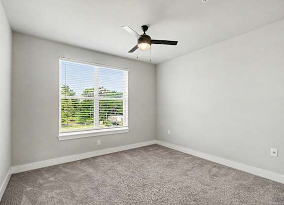 A room with a ceiling fan and a window overlooking a green landscape.