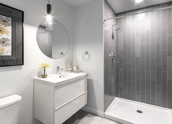 Steelcote Crossing bathroom with white cabinetry, white quartz countertops, large circular mirror and walk in shower with tile surround at Steelcote Square, Missouri