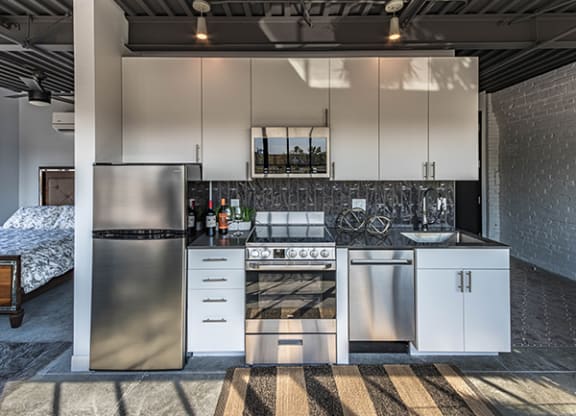 Steelcote Crossing kitchen with white cabinetry, black quartz countertops, stainless steel appliances, black tile backsplash and concrete floors at Steelcote Square, Missouri, 63103