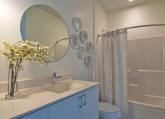 Steelcote Lofts bathroom with white cabinetry and white quartz countertops. Large circular mirror and tile at Steelcote Square, St. Louis, 63103