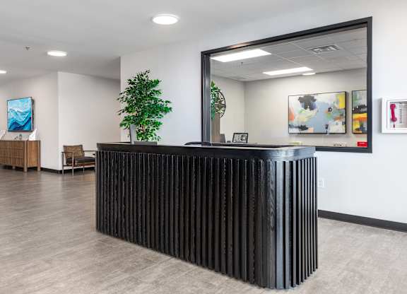 A black reception desk with a mirror above it in a room with wooden floors.