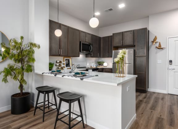 Modern kitchen with designer lighting, quartz countertops, dark cabinetry and stainless steel appliances  with countertop with seating  at Chapter at the Streets of St Charles, Saint Charles, 63303