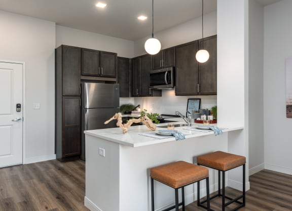 Modern kitchen with designer lighting, dark cabinetry, stainless steel appliances and counter with seating  at Chapter at the Streets of St Charles, Saint Charles, 63303