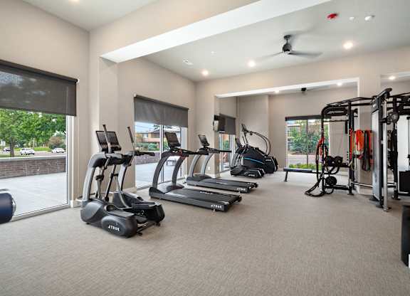 A spacious gym with a variety of equipment including treadmills, elliptical machines, and weight machines at The Oliver Apartments, Olivette, MO, 63132