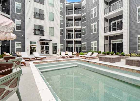 A pool surrounded by chairs and umbrellas in front of a building at The Oliver Apartments, Missouri