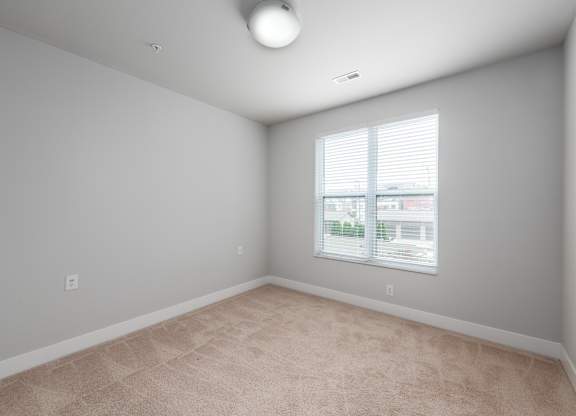A room with a window and a carpeted floor.
