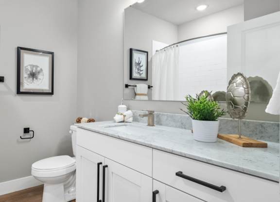 A white bathroom with a toilet, sink, and mirror at The Oliver Apartments, Olivette, MO
