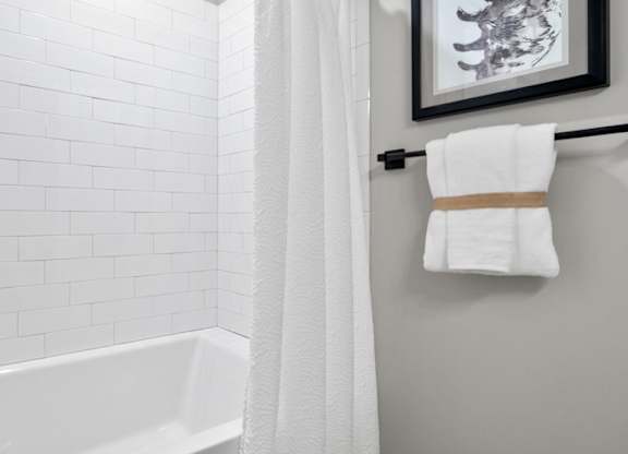 A white bathroom with a white tub and a white shower curtain at The Oliver Apartments, Olivette, MO, 63132