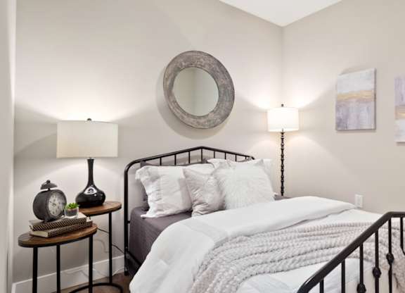 A bedroom with a bed, nightstand, lamp, and a plant at The Oliver Apartments, Olivette