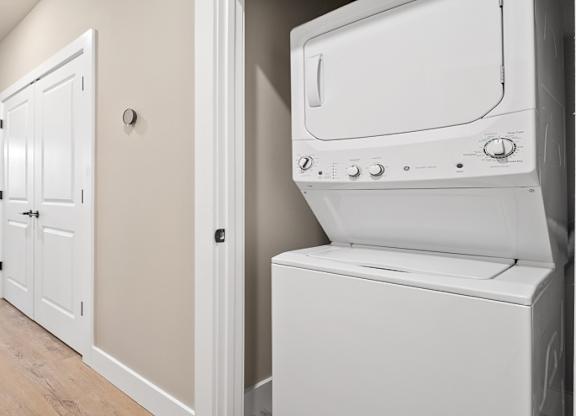 A white washing machine is in a laundry room at The Oliver Apartments, Missouri, 63132