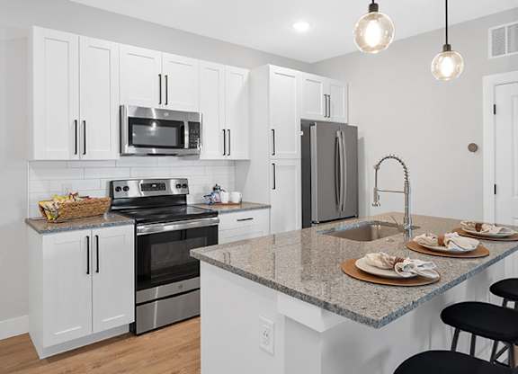 A kitchen with white cabinets and a granite countertop at The Oliver Apartments, Olivette