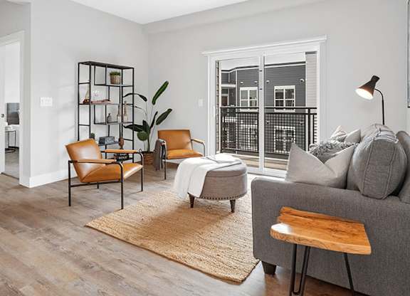 A living room with a grey couch, a brown chair, a white chair, a wooden table, a rug, and a plant at The Oliver Apartments, Olivette, 63132