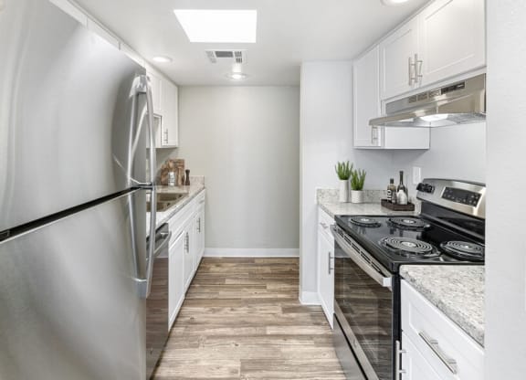 Pet-Friendly Affordable Apartments in East Tucson, AZ - Lakeside Casitas - A Kitchen With White Cabinets, Stainless Steel Appliances, Recessed Lighting, And Wood Style Flooring.