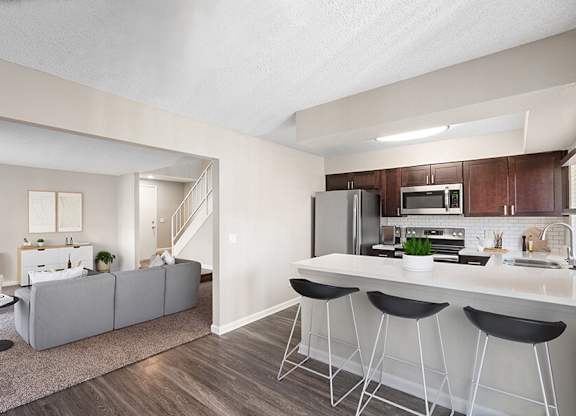 Model Kitchen with Dark Wood Cabinets, Wood-Style Flooring and View of Living Room at Horizon Apartments located in Santa Ana, CA.