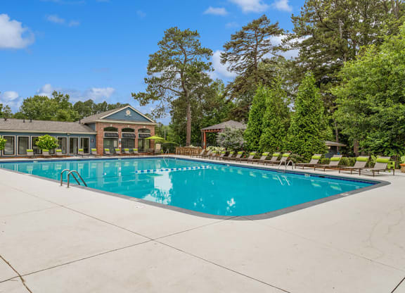 Resort-style swimming pool with lounge chairs and trees in the background